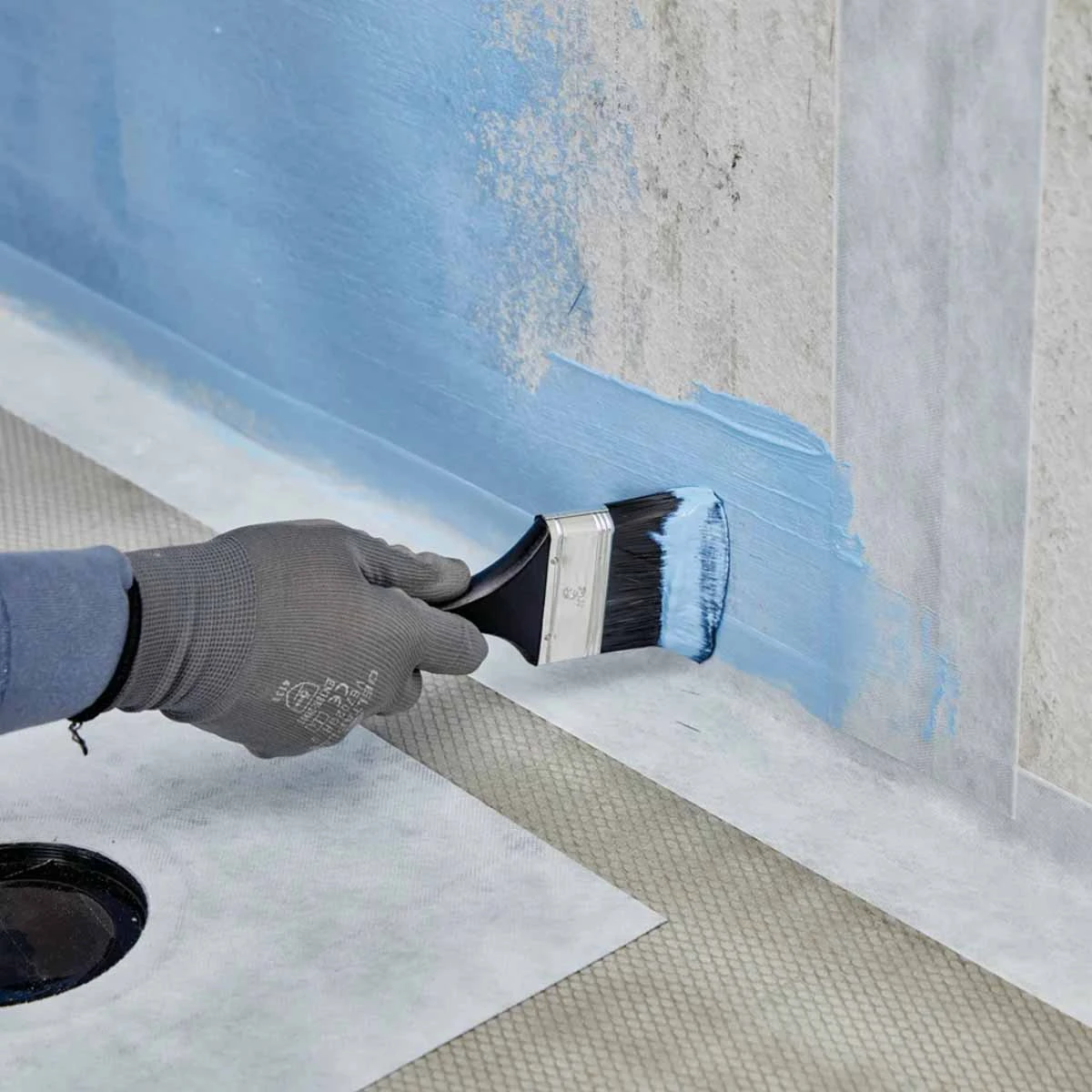 Blue waterproofing membrane being brushed along a wall and floor junction